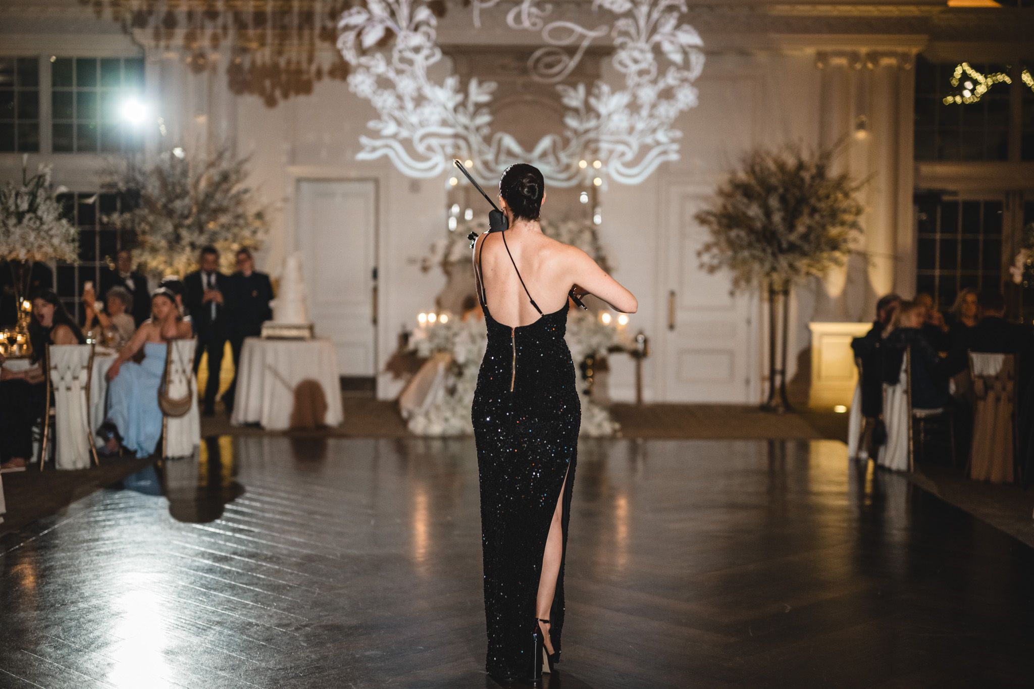 Elegant woman in black backless gown performs at luxury wedding reception in ornate ballroom.