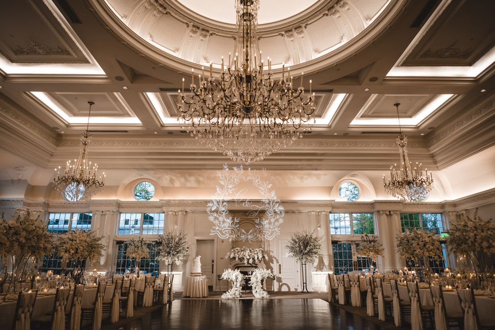 An elegant wedding reception ballroom features grand crystal chandeliers and tall floral centerpieces.