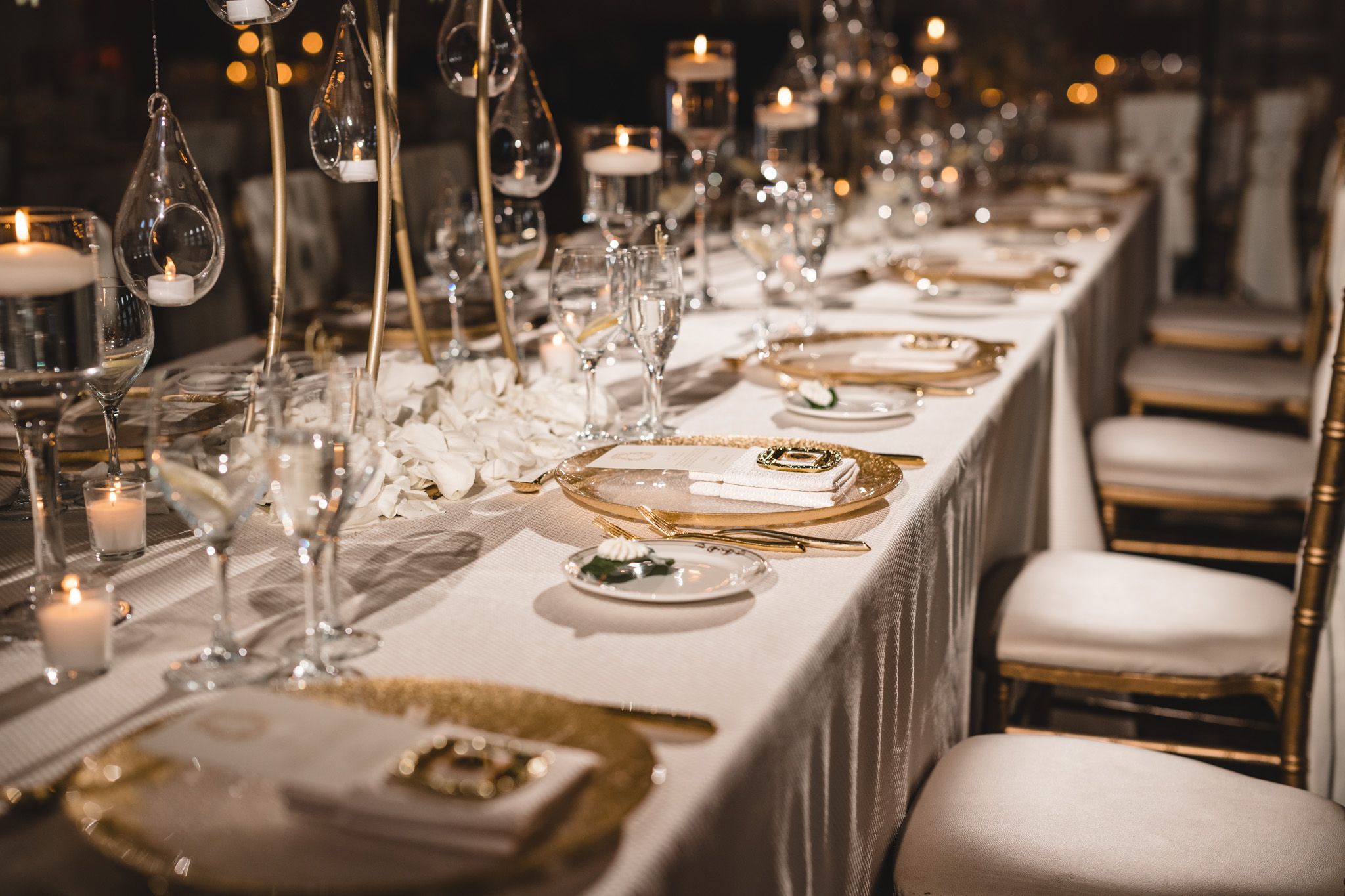 Luxurious wedding reception table set with gold chargers, crystal glassware, and candlelight.
