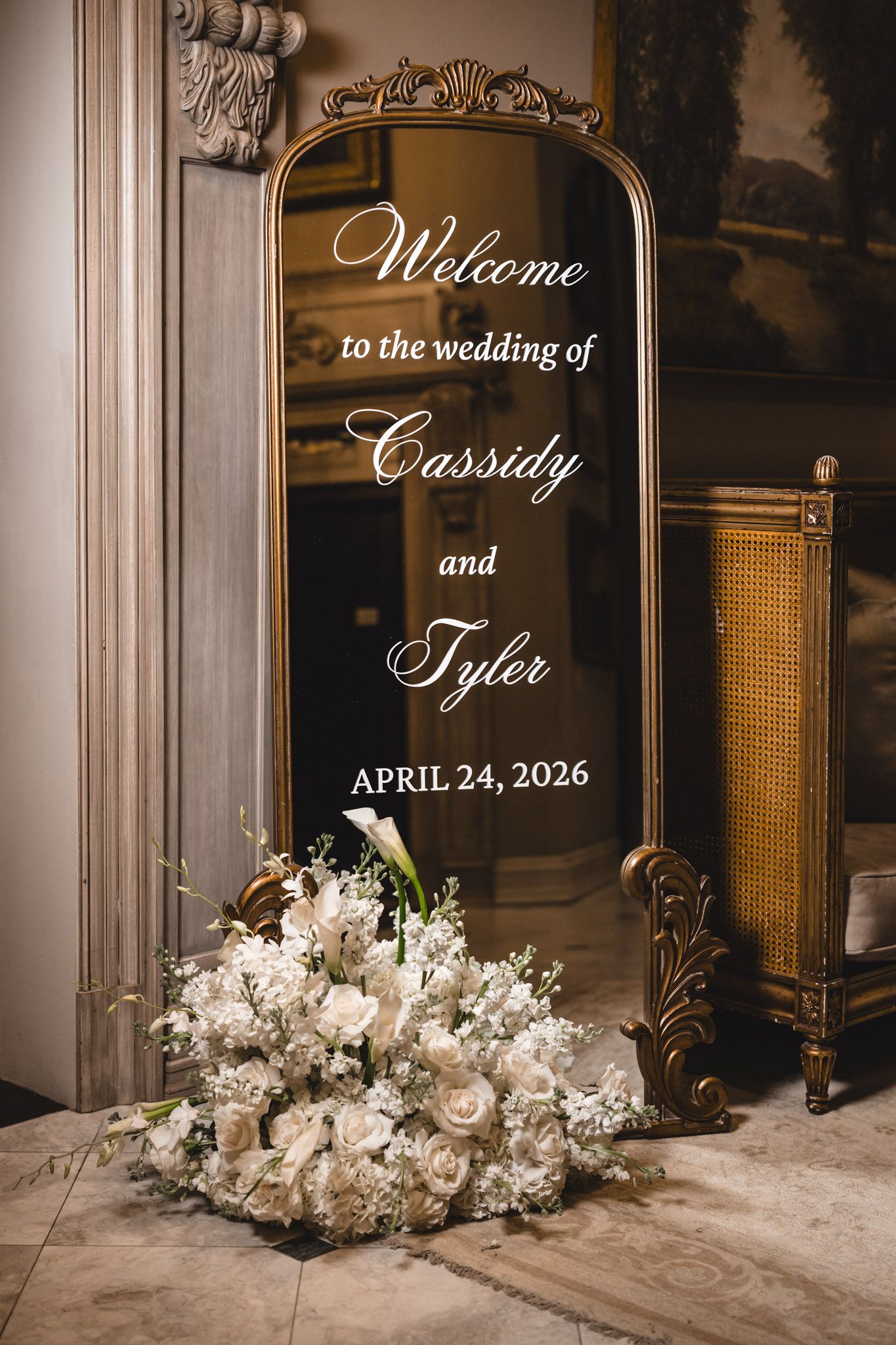 Gold mirror wedding welcome sign for Cassidy and Tyler with white floral arrangement below.