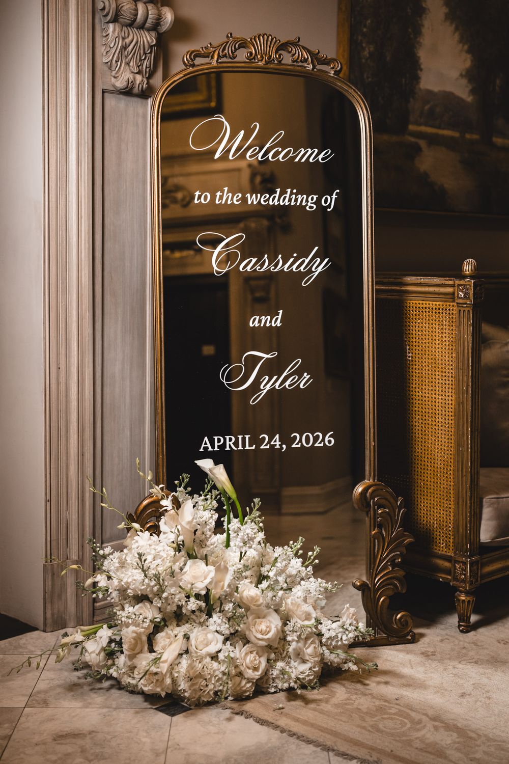 Gold mirror wedding welcome sign for Cassidy and Tyler with white floral arrangement below.