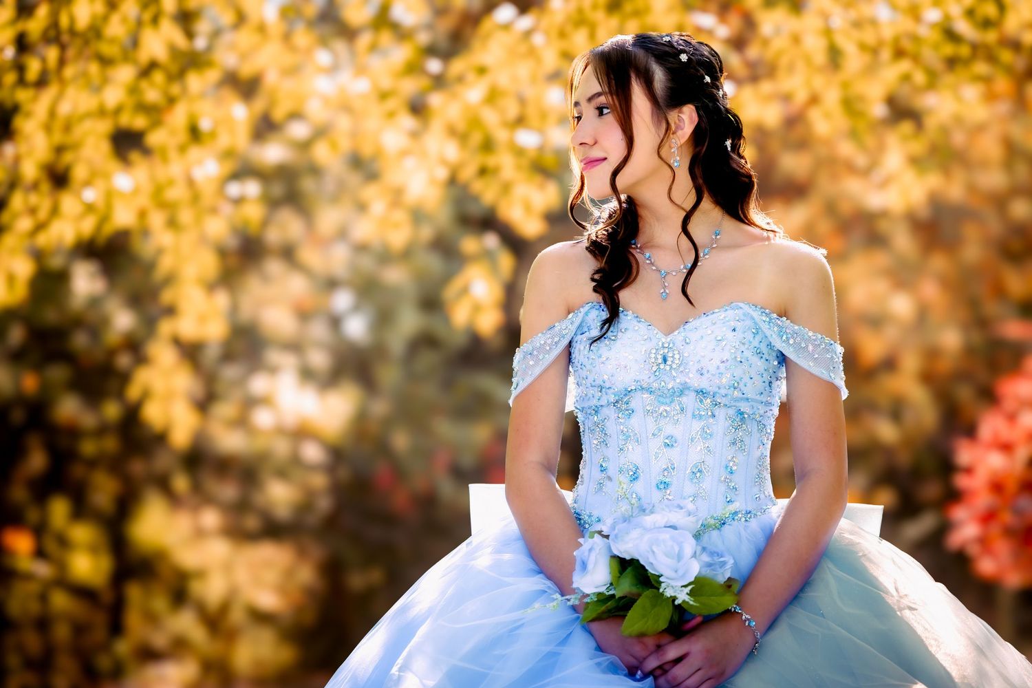 Person wearing a white long-sleeved dress leans against a wooden railing in an autumn setting.