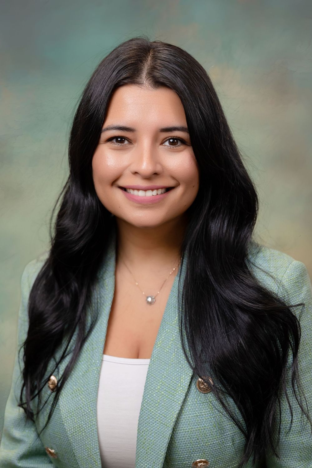 Professional headshot of a young woman with long black hair wearing a mint green blazer and delicate necklace.