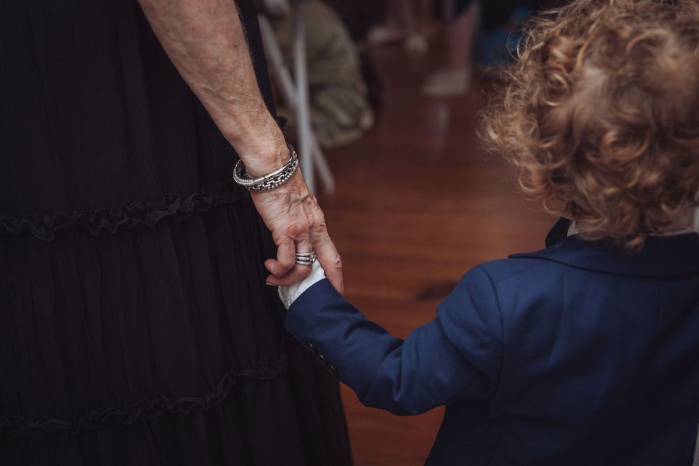 Adult holding hands with a young curly-haired child in a blue suit at a wedding reception.