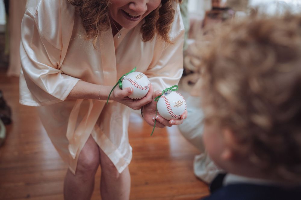 Woman in silk robe showing two baseballs to a curly-haired child during a wedding preparation moment.