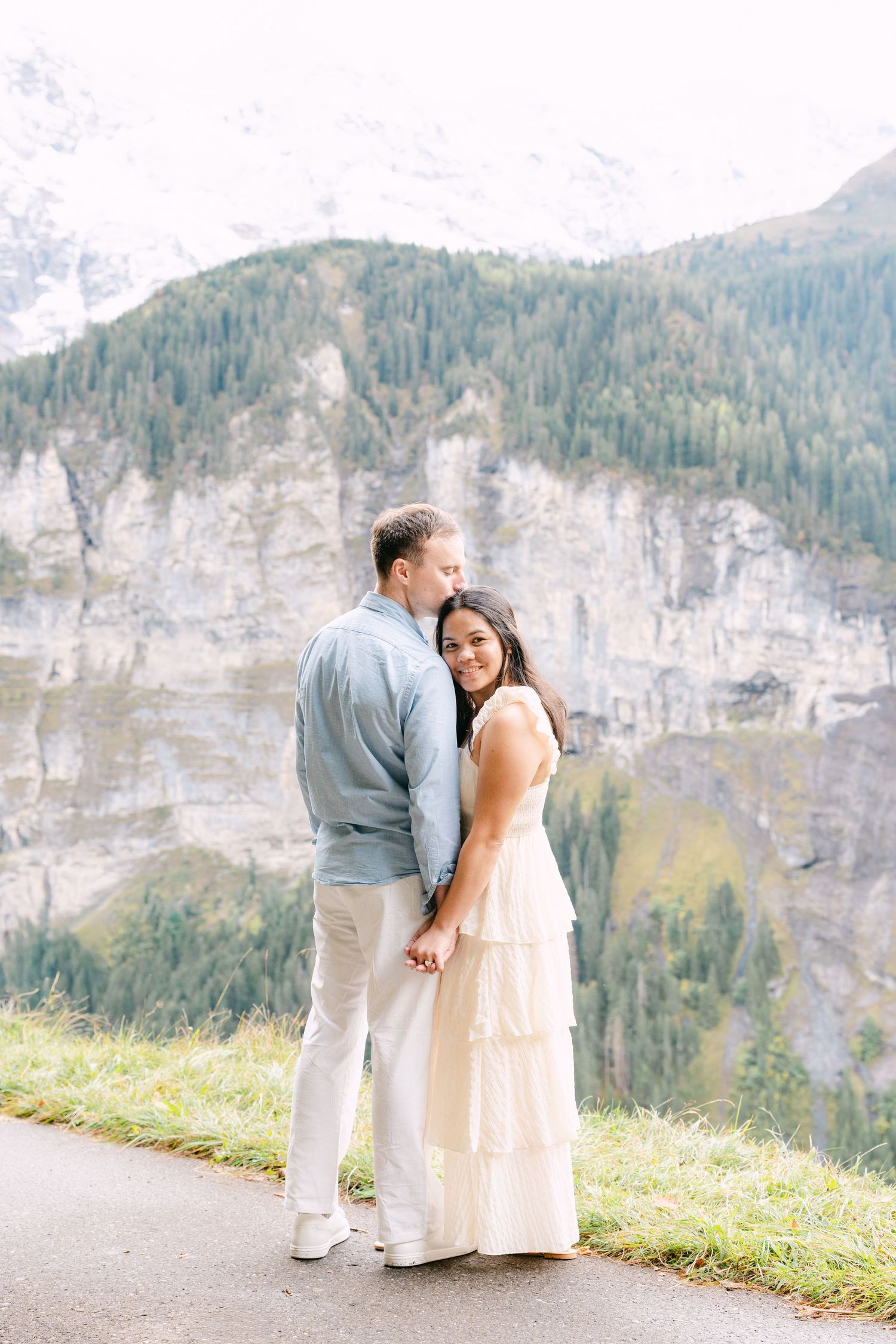 Couple in white outfits sharing a romantic moment against stunning mountain cliffs and scenic valley landscape in Mürren, Switzerland.