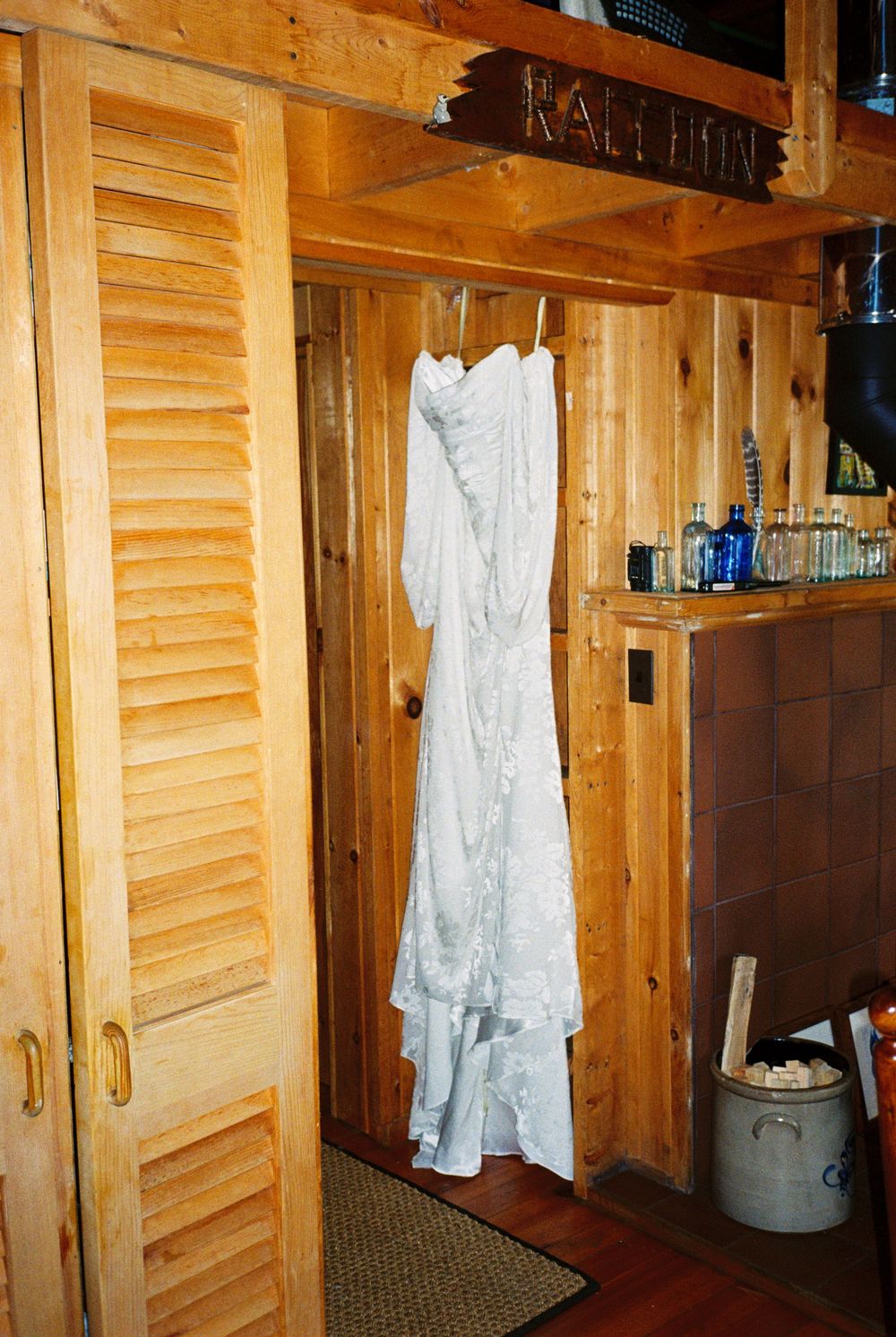The bride's wedding dress hangs in their family camp cottage while she gets ready for the ceremony. Her mother and maid of honor join her.