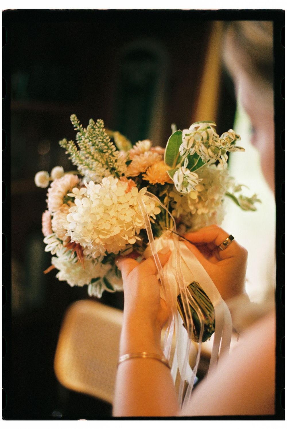 The maid of honor holds the bride's bouquet and carefully attaches ribbon around the stems before heading to the wedding ceremony in Maine.