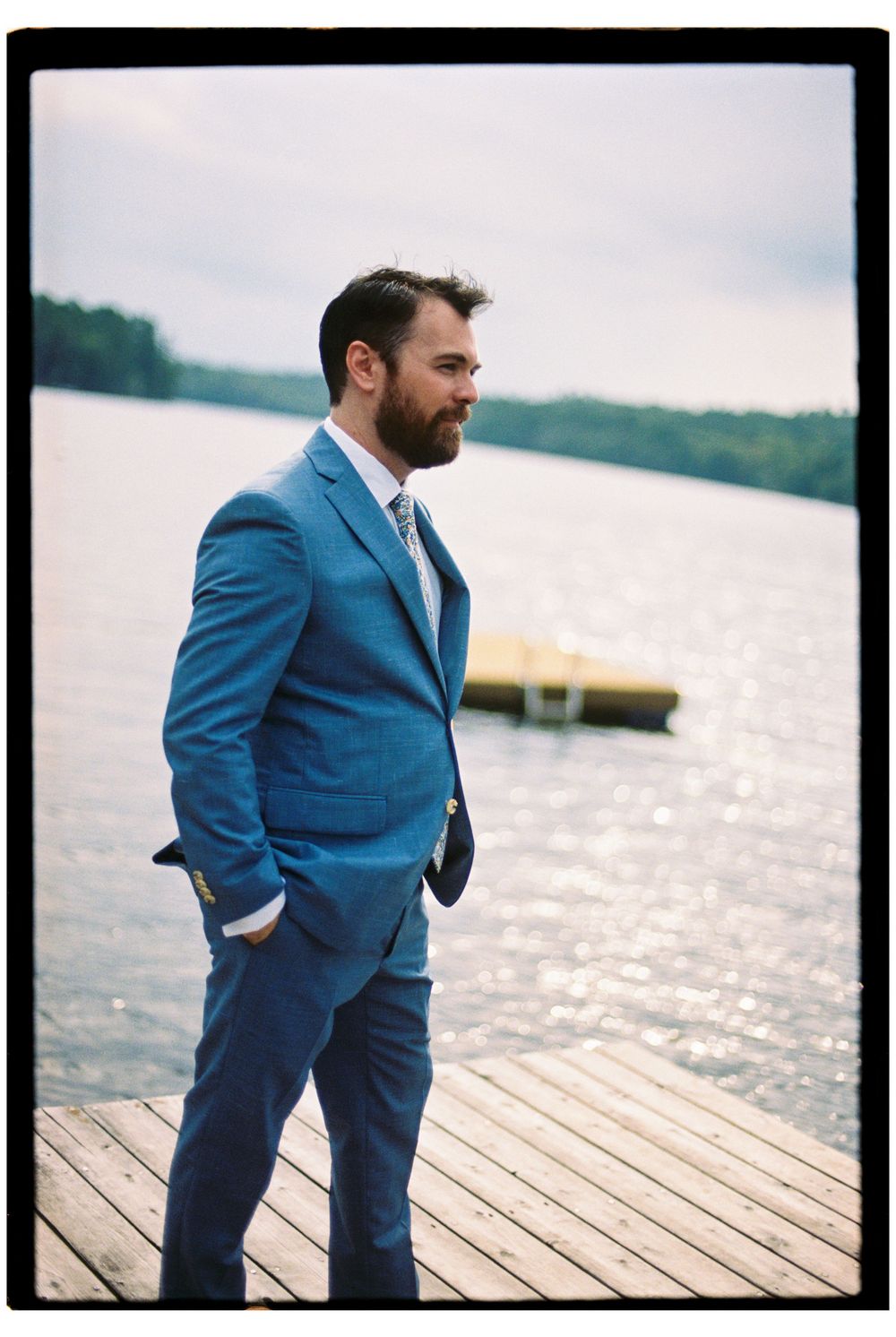 Portrait of the groom at the end of the dock before seeing his bride in her wedding gown for the first time. He happily gazes at the water.