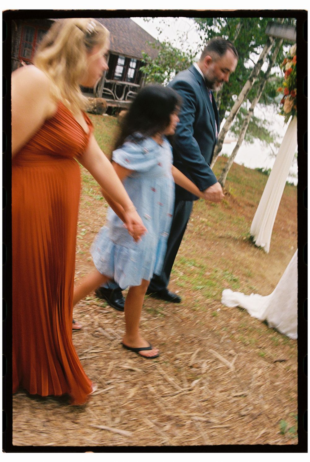 The brother of the groom, his daughter and the maid of honor hold hands, swinging their arms and walking together before wedding in Maine.