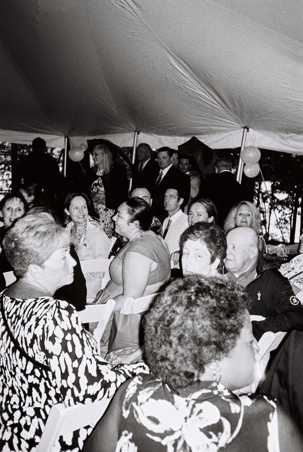 A sea of wedding guests wait for the bride to arrive under a tent on black and white film. The rain is pouring outside but the love is real.