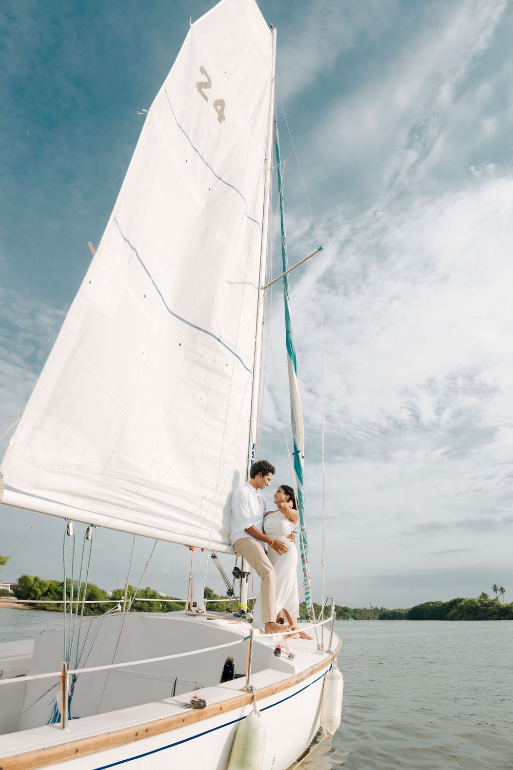A sailboat glides across calm waters under cloudy skies with a couple enjoying a romantic moment.