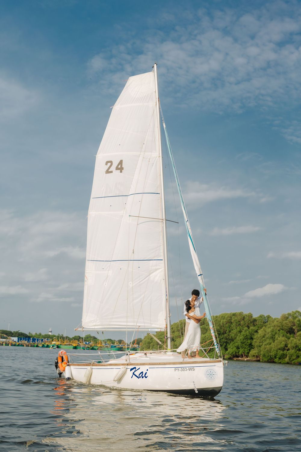 A white sailboat glides across blue waters near a lush shoreline on a sunny day.