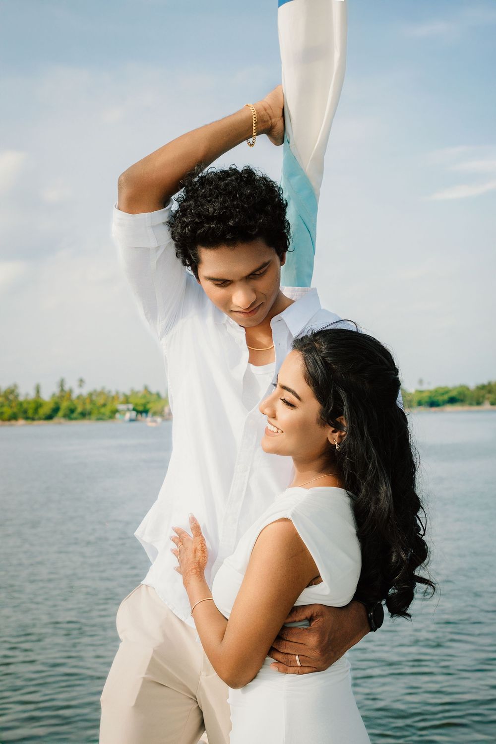 A romantic couple embraces and laughs together during a waterfront photoshoot in white attire.