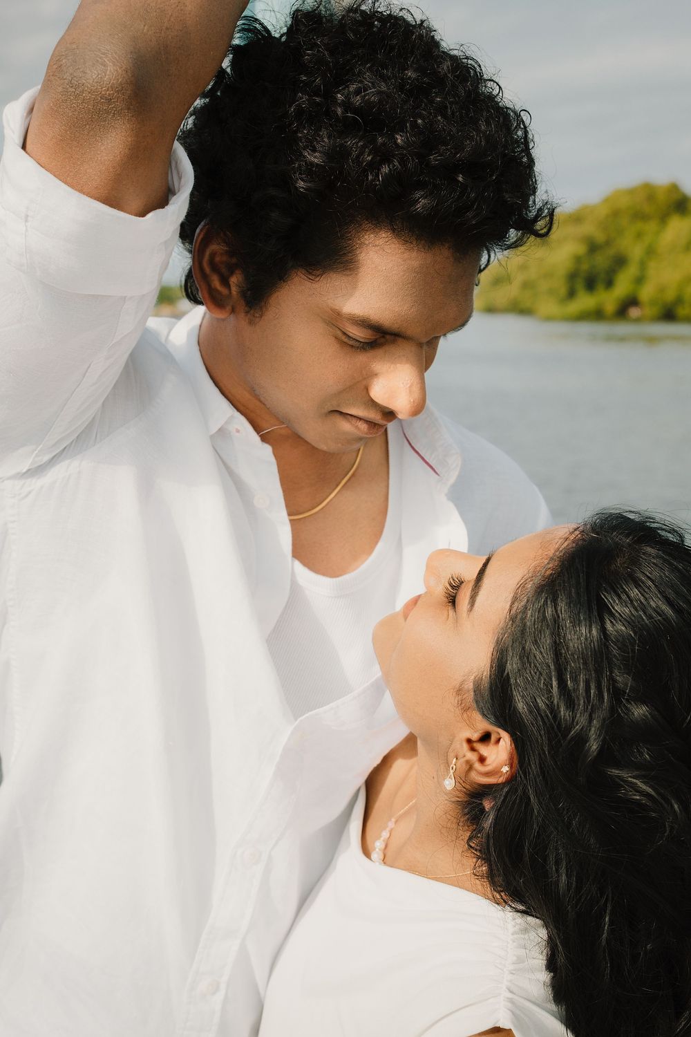 A romantic couple in white clothing embraces on a boat against a waterfront backdrop.