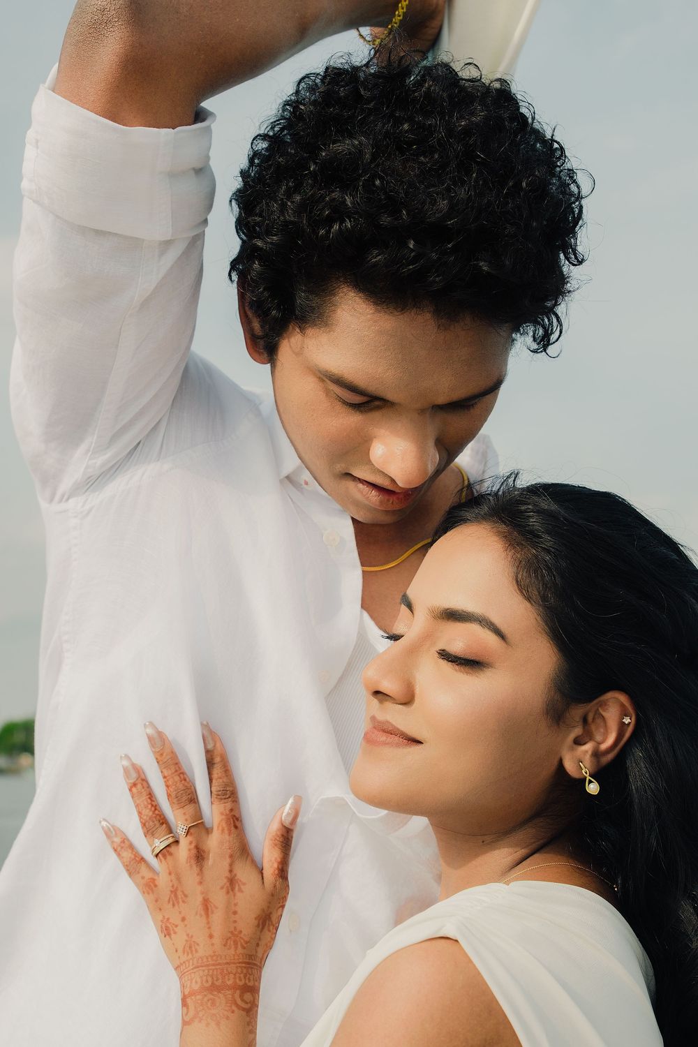 A romantic couple in white clothing embraces tenderly against a light background.