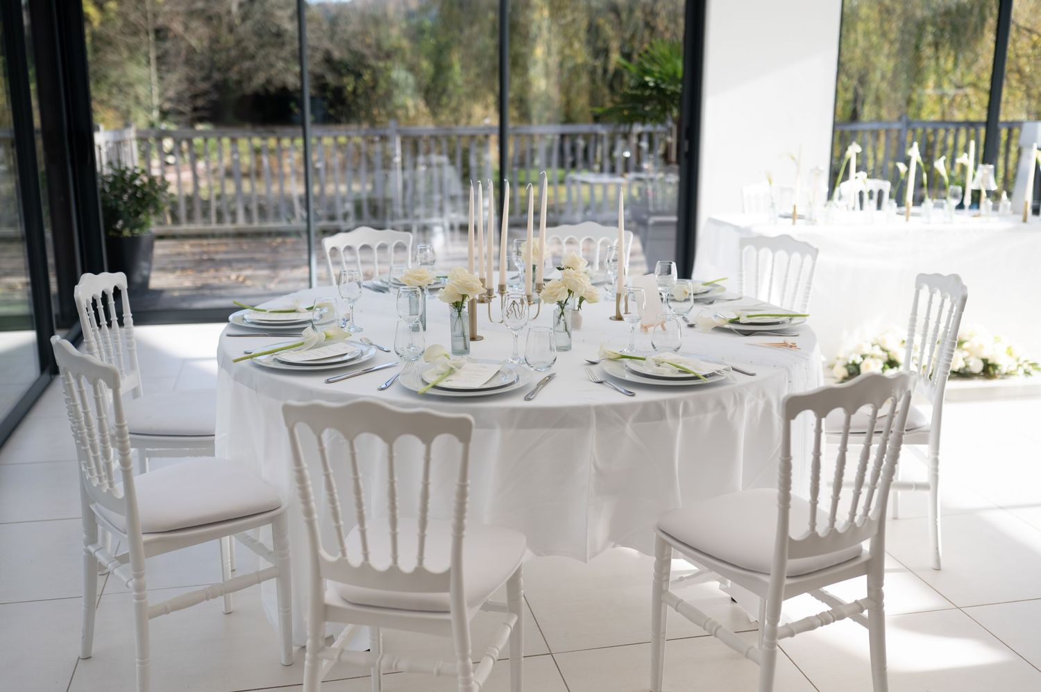 Élégante table à manger ronde blanche avec décors et chaises blanches dans une pièce lumineuse avec vue sur la fenêtre.