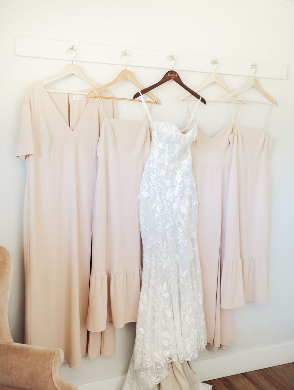 Row of blush pink bridesmaid dresses and a white lace wedding gown hanging on a clothing rack.