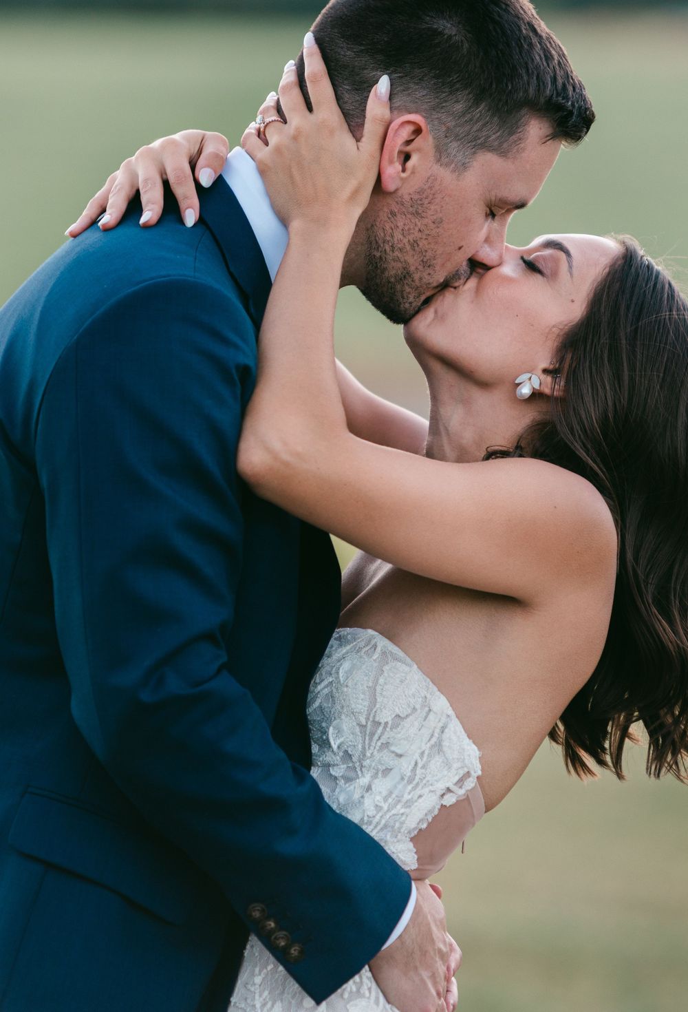 A romantic wedding couple shares an intimate kiss outdoors in formal attire.