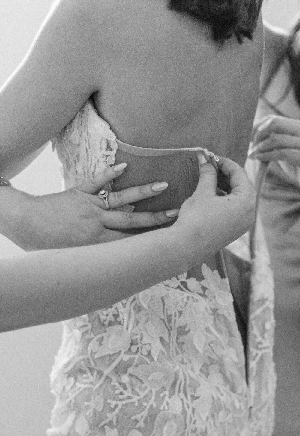 Close-up sequence showing hands adjusting and fitting a delicate white lace dress with floral patterns.