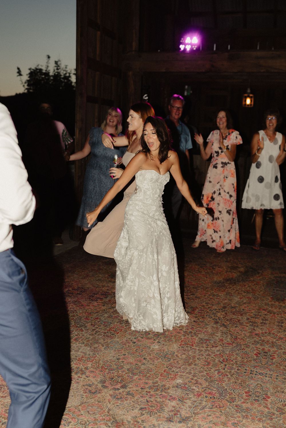 Wedding reception dance floor with guests celebrating in a dimly lit barn.