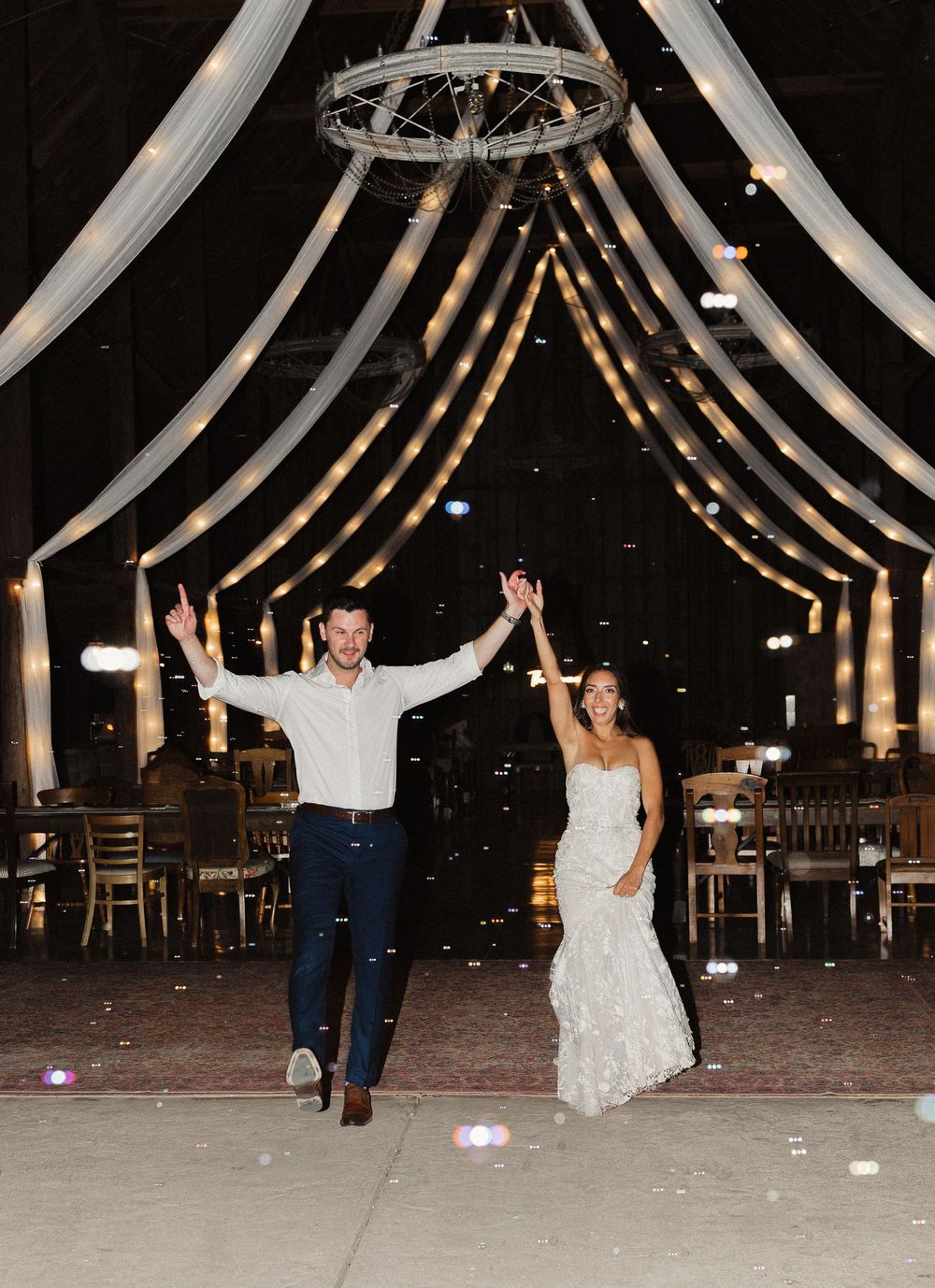 Couple dances joyfully under illuminated white fabric drapes and string lights at an elegant wedding reception.