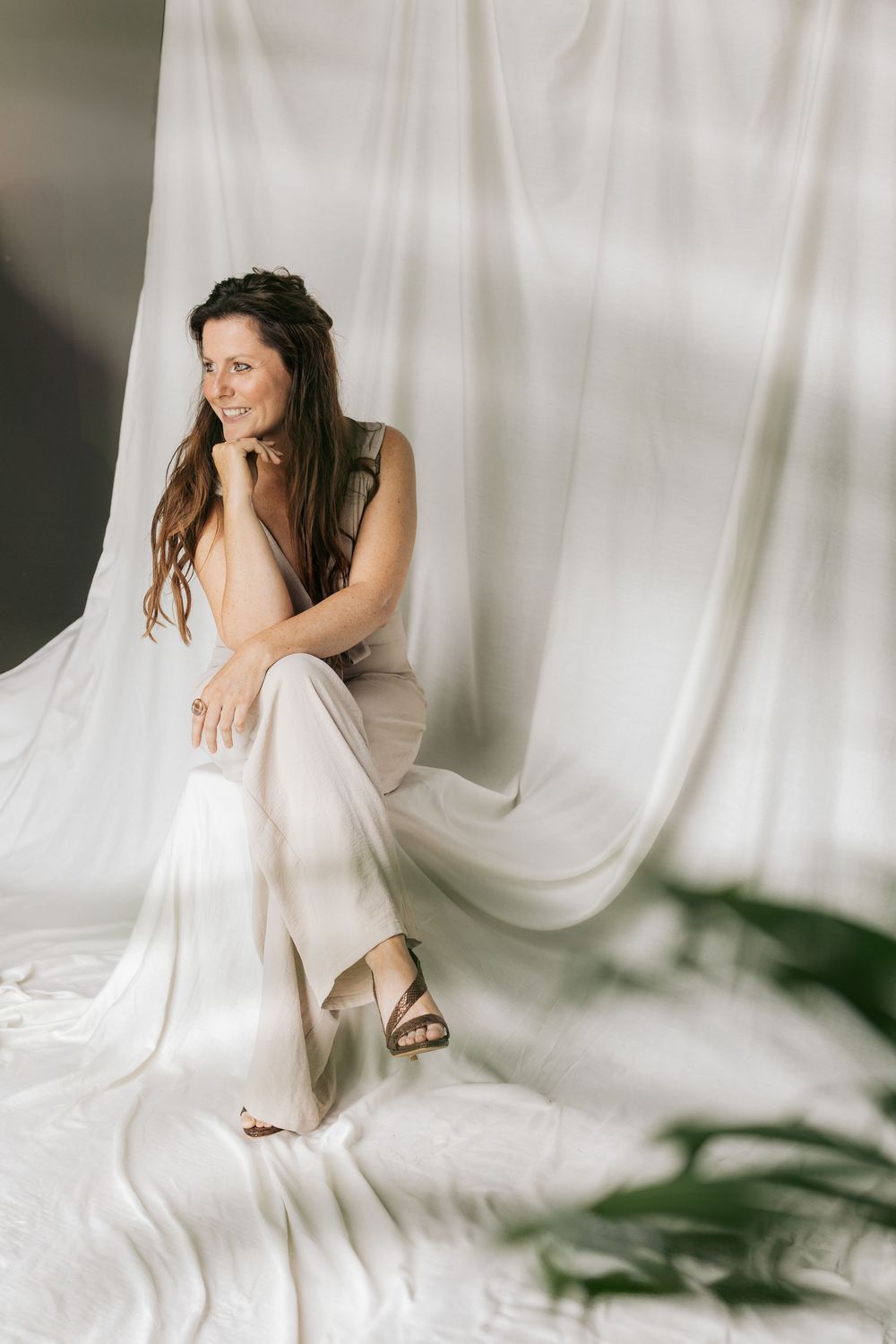 Woman in white outfit sitting gracefully against flowing white fabric backdrop.