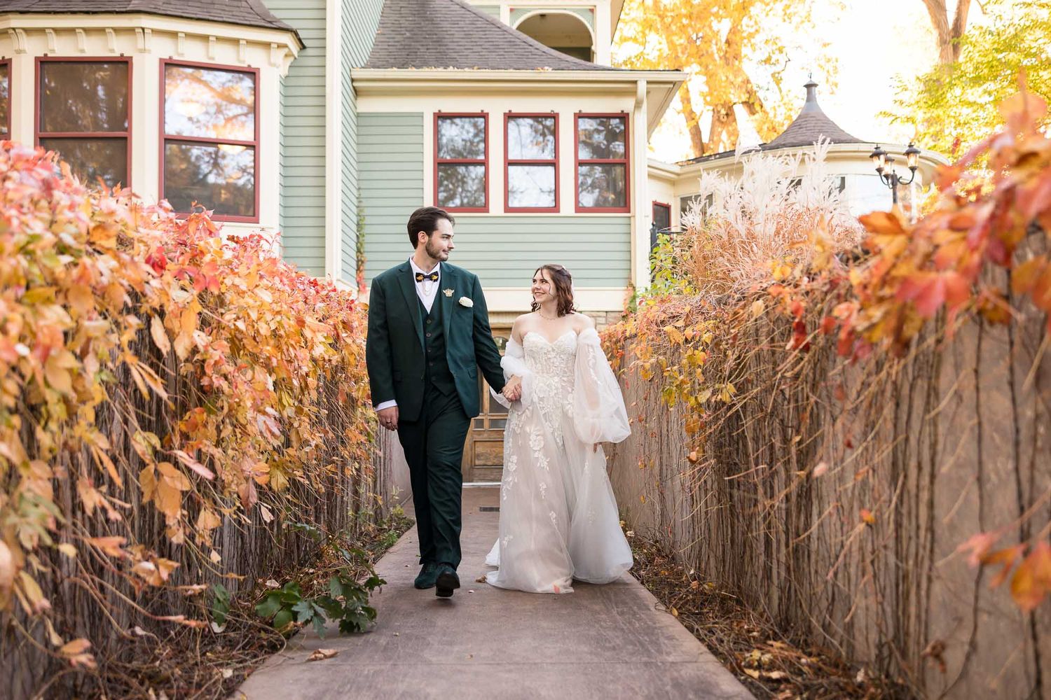 A couple walks together along a rustic wooden fence surrounded by autumn foliage at golden hour.