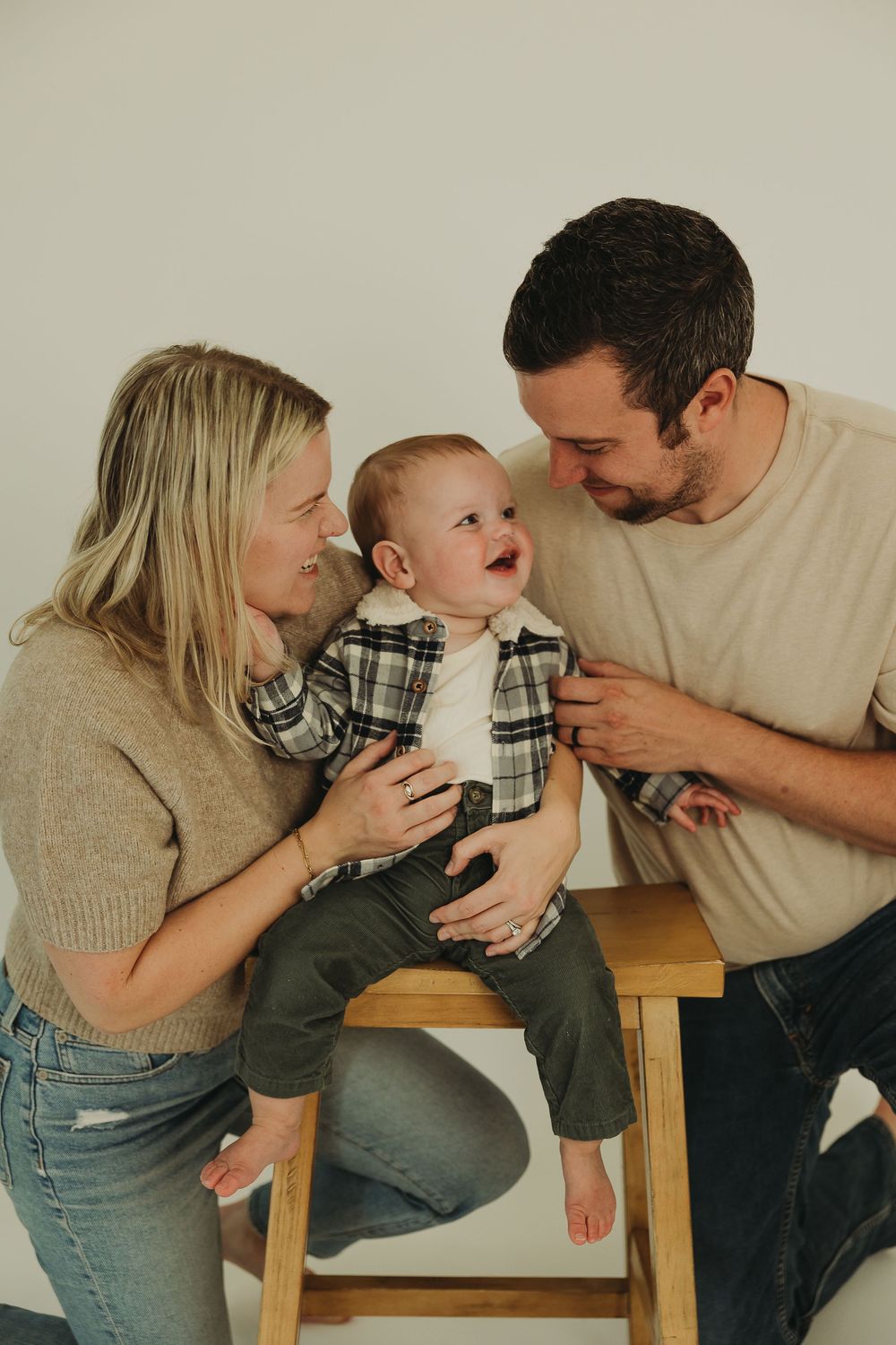 A family of three shares playful moments together while sitting on a wooden bench in casual attire.