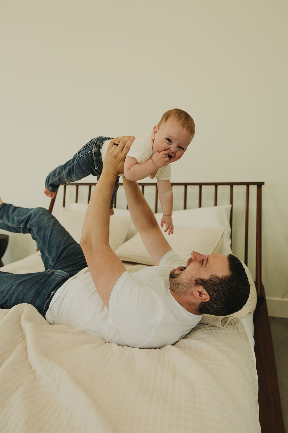 A tender moment showing an adult lying on a bed playing with and lifting up a baby in a sequence of photos.