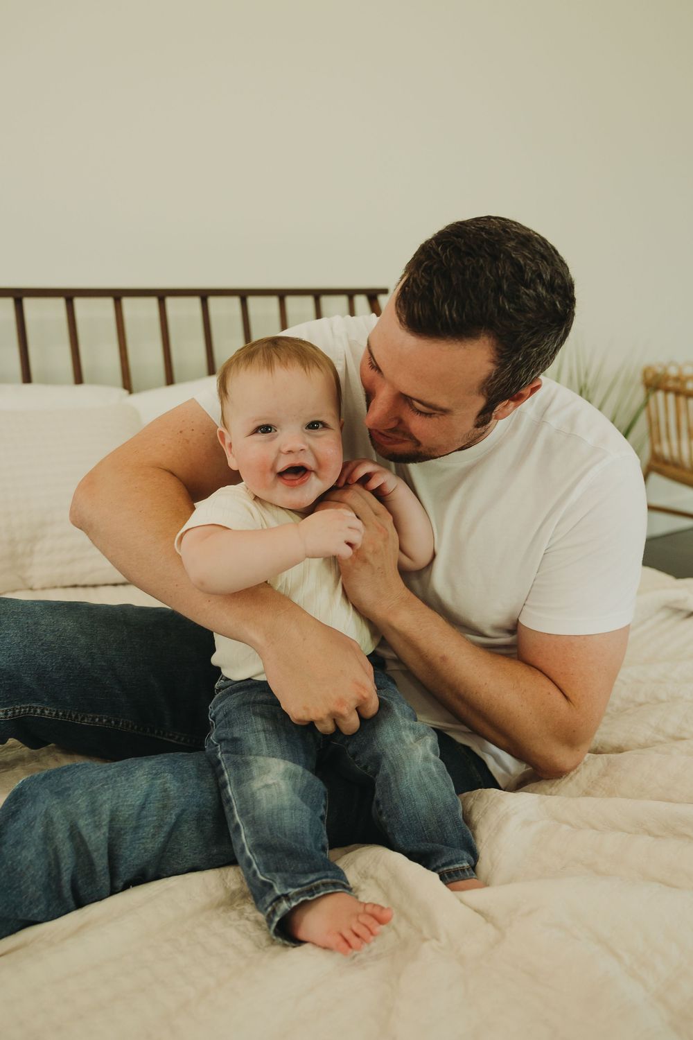 A playful moment captured on a bed as a parent and baby interact with joyful expressions.