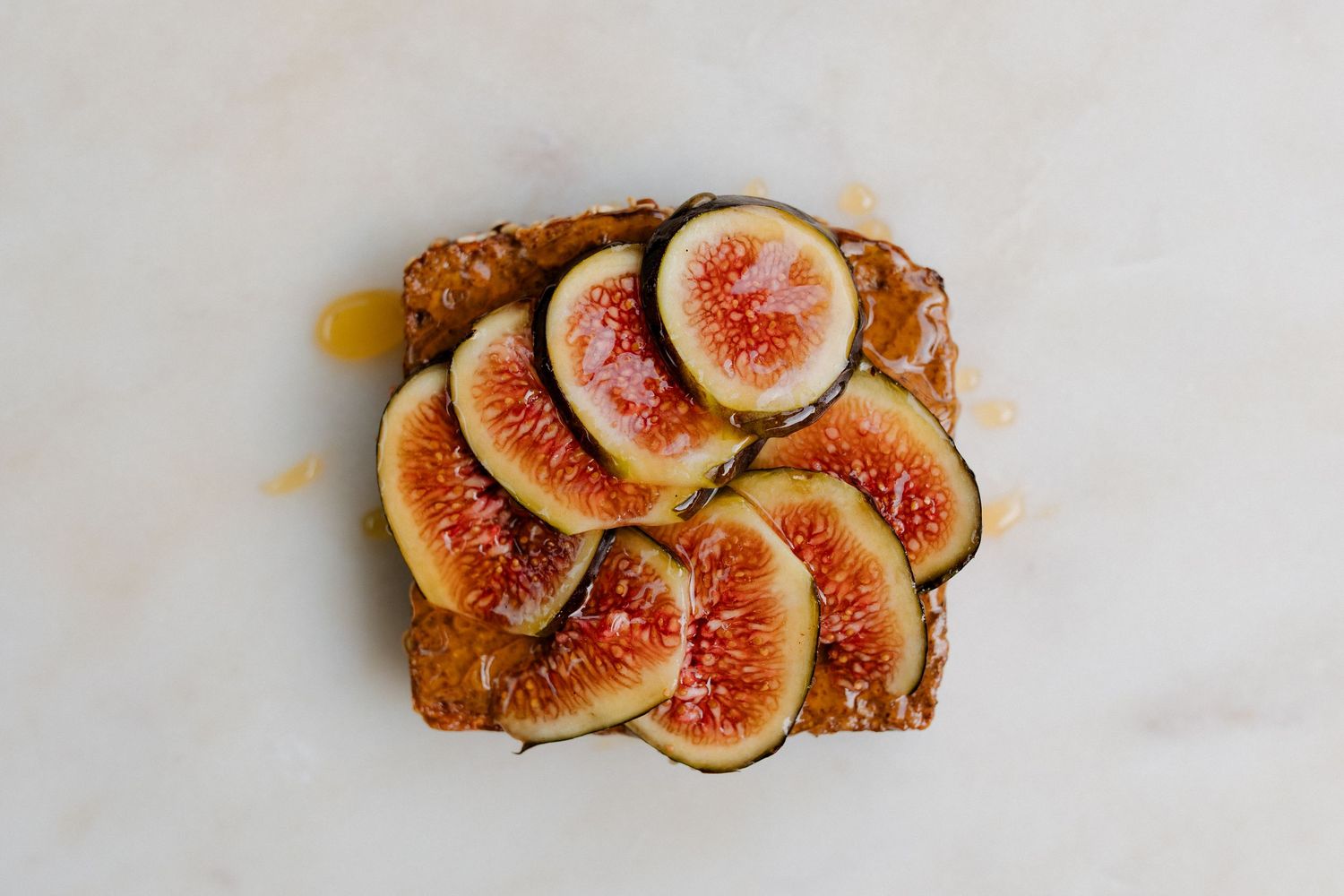Fresh sliced figs arranged artistically on toast with almond butter, on a white marble surface.