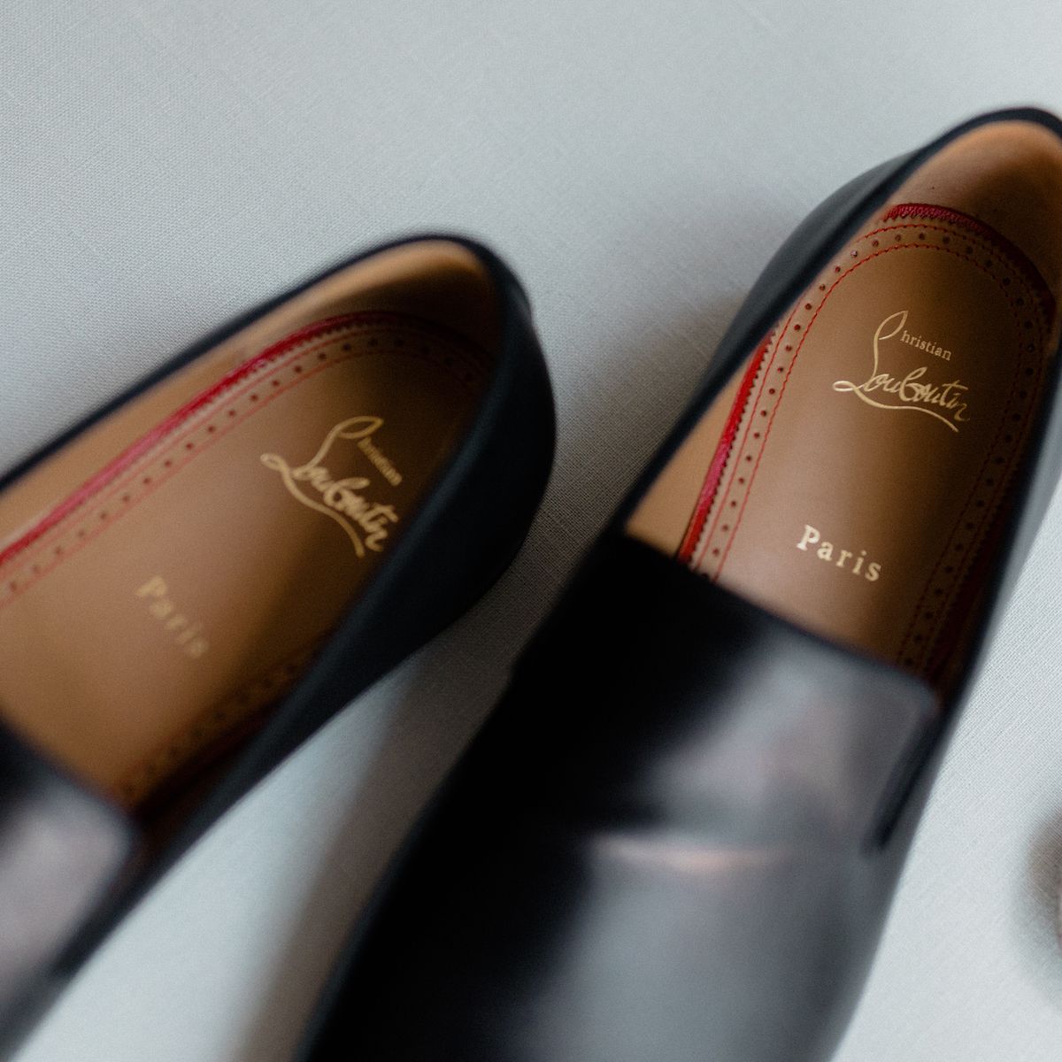 Close-up detail of black leather shoes showing Louboutin brand logo and stitching.