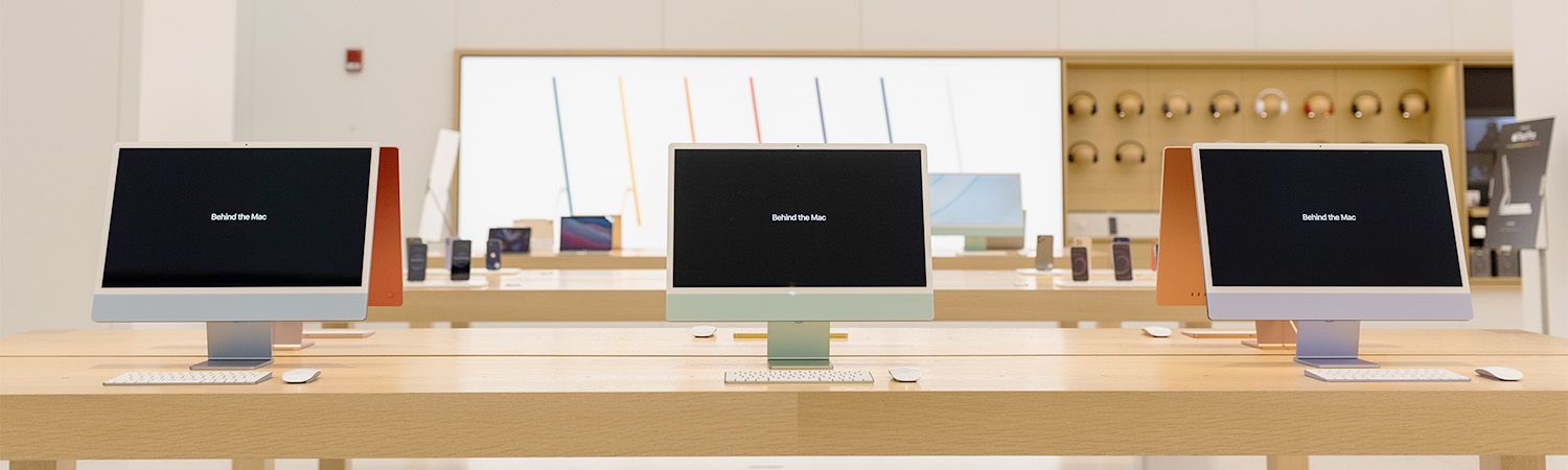Row of digital screens mounted on a wooden table in a modern retail space at Apple Store.