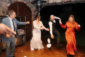 Wedding party guests dance and celebrate on a wooden dance floor at an indoor reception venue.