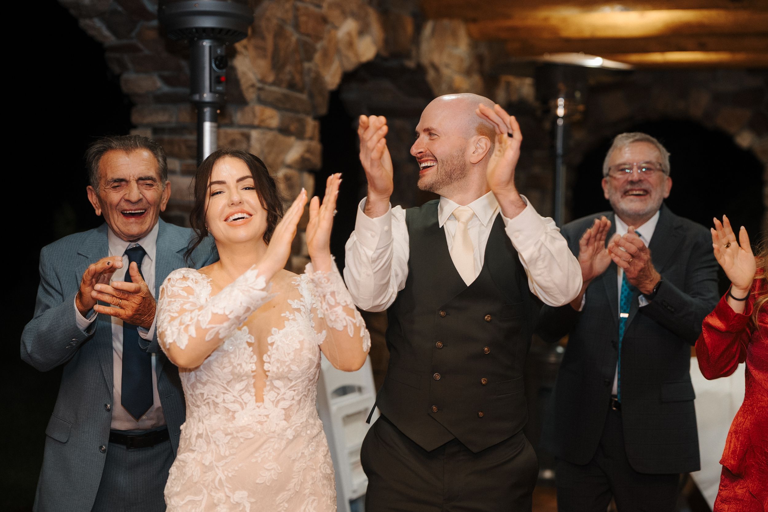 A wedding couple and guests dance joyfully at a reception with warm lighting and festive atmosphere.