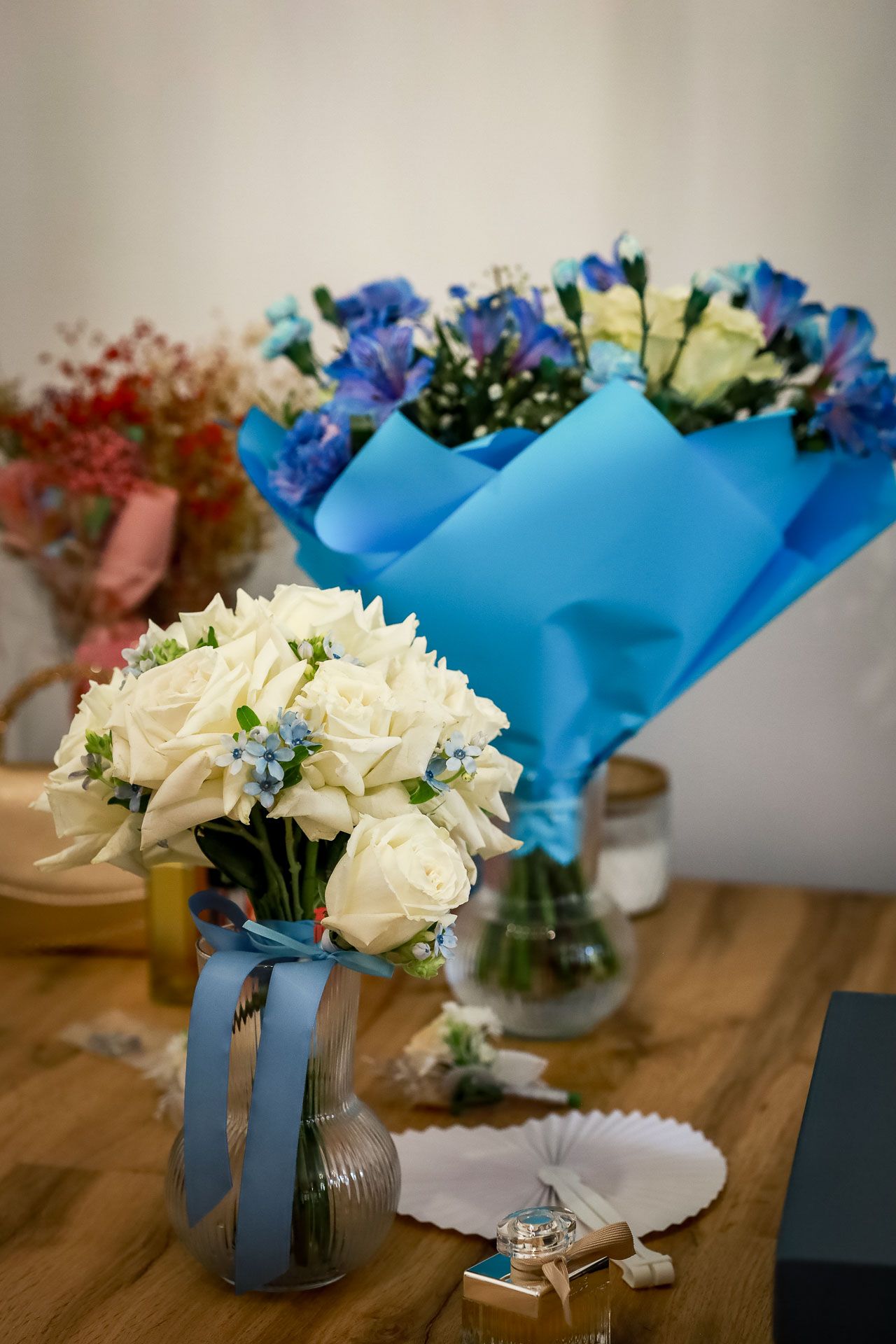 White roses and blue flowers arranged in glass vases on a wooden table.