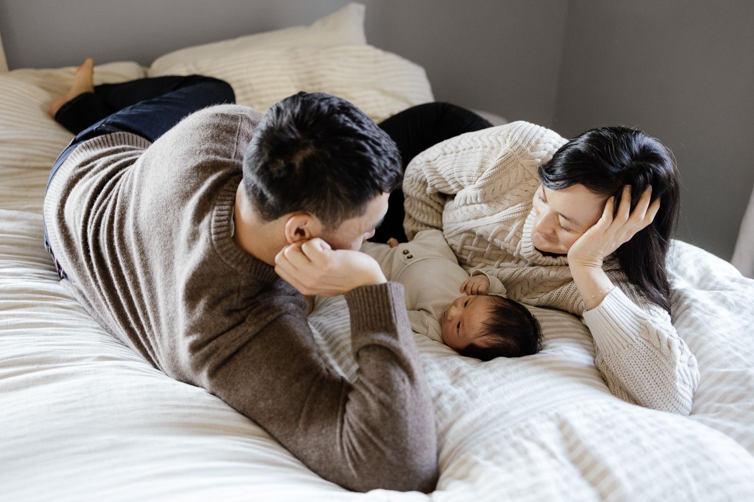 A family of three lays on their bed at their in-home newborn photography session with Cindy Tucey Photography