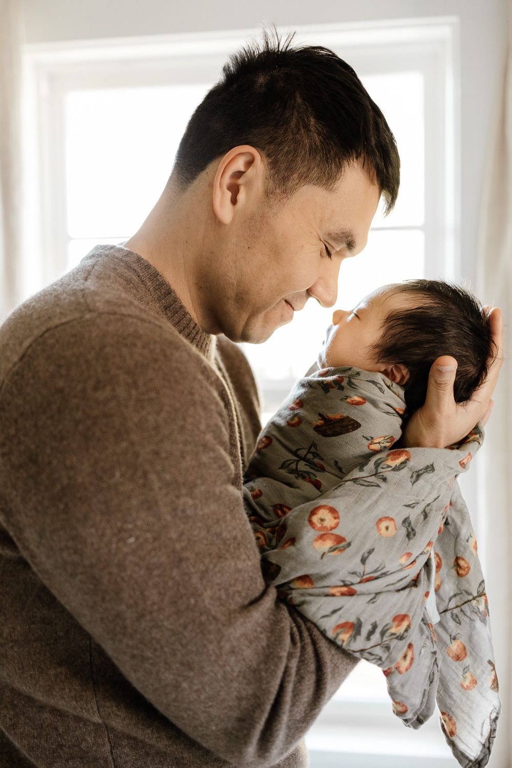 Dad puts his baby near his nose while smiling at a newborn photo session in the Bay Area