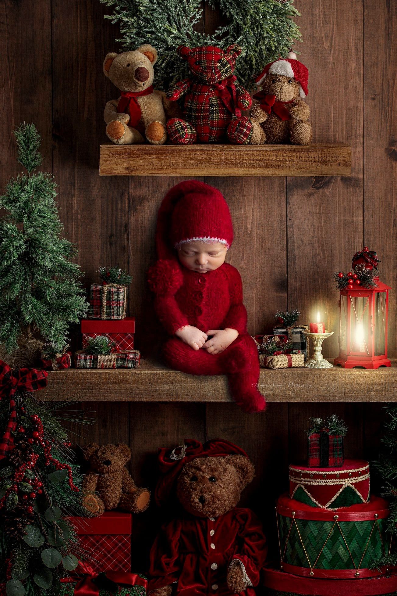Cozy Christmas scene with rustic wooden backdrop, red decorations, teddy bears, and glowing candlelight.