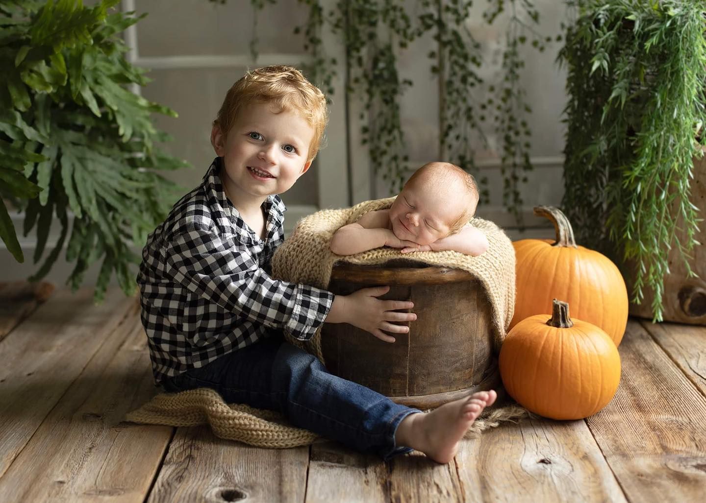 A child and pumpkin on a rustic wooden porch with greenery and autumn decor.