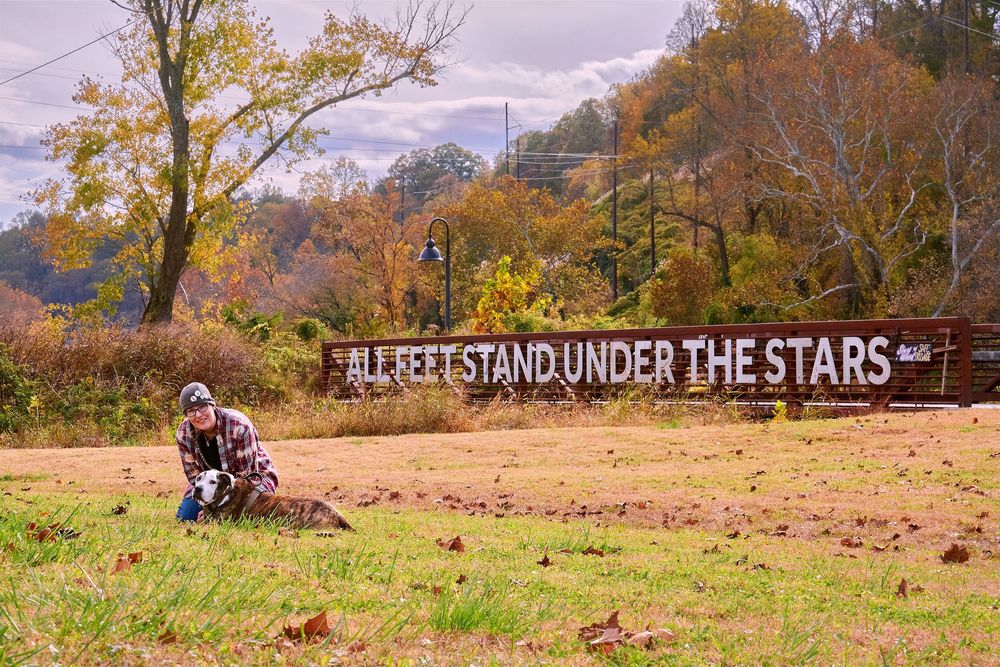 Rustic outdoor photo session in autumn field with wooden fence and 'Stand Under the Stars' sign at sunset.