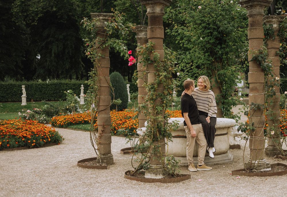 A stone archway with climbing vines frames a garden path surrounded by vibrant orange flowers and greenery.
