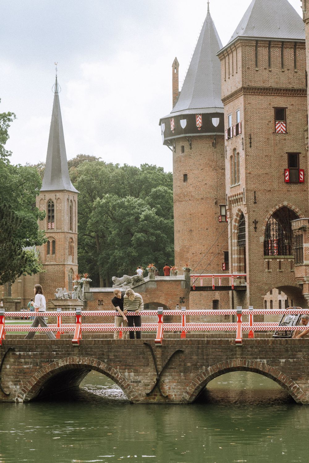 Historic stone bridge with Gothic towers and turrets spans a canal at the Minnewater Park in Bruges, Belgium.