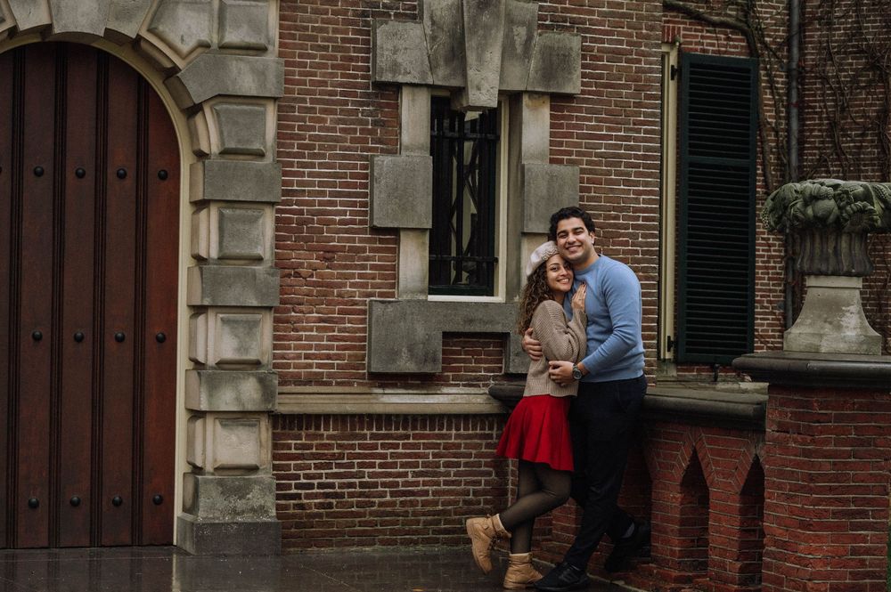 A couple embraces while standing outside a historic brick building with ornate architectural details.