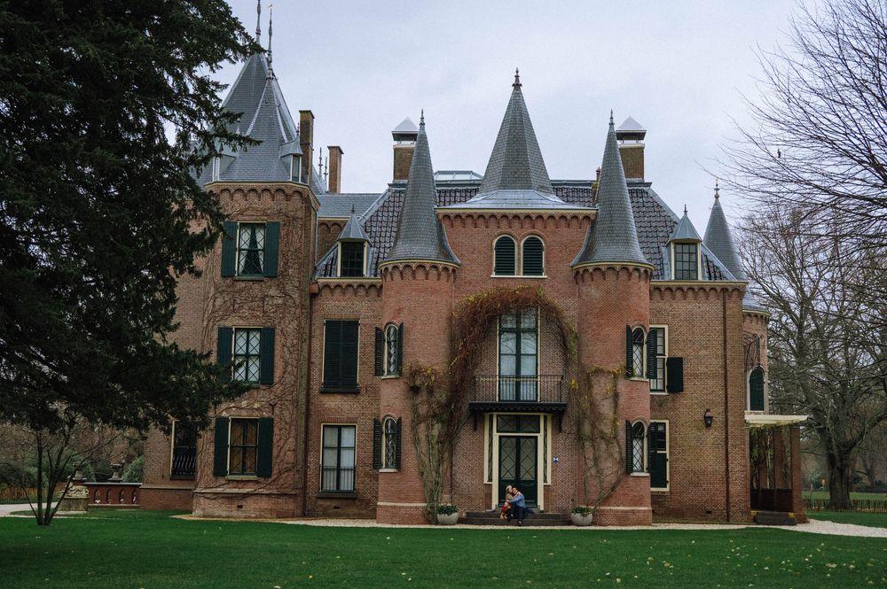 Gothic Revival mansion with steep gables and ornate architectural details sits on a landscaped lawn in winter.