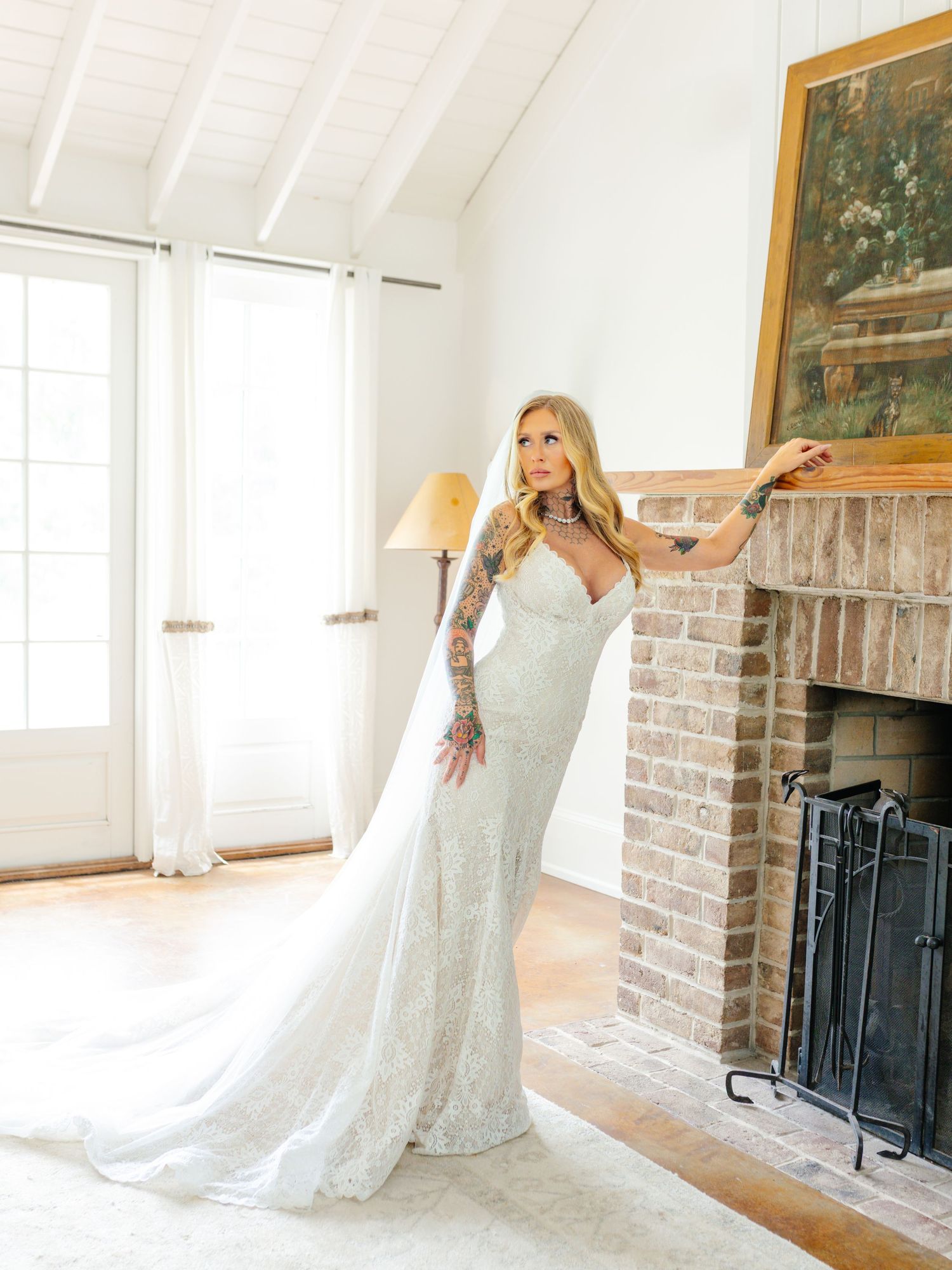 Bride in lace wedding gown twirls and poses in bright white room with brick fireplace.