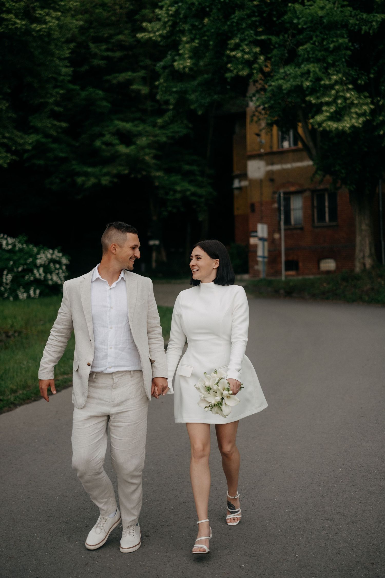 Couple in all-white outfits walking together on path near historic building.