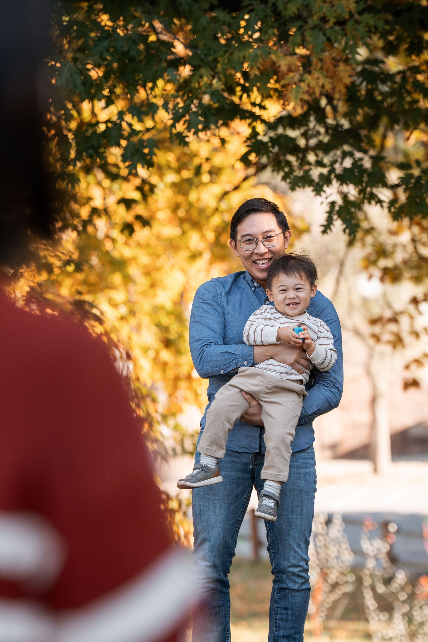 A playful autumn photoshoot in a park with golden foliage and sunlight filtering through the trees.