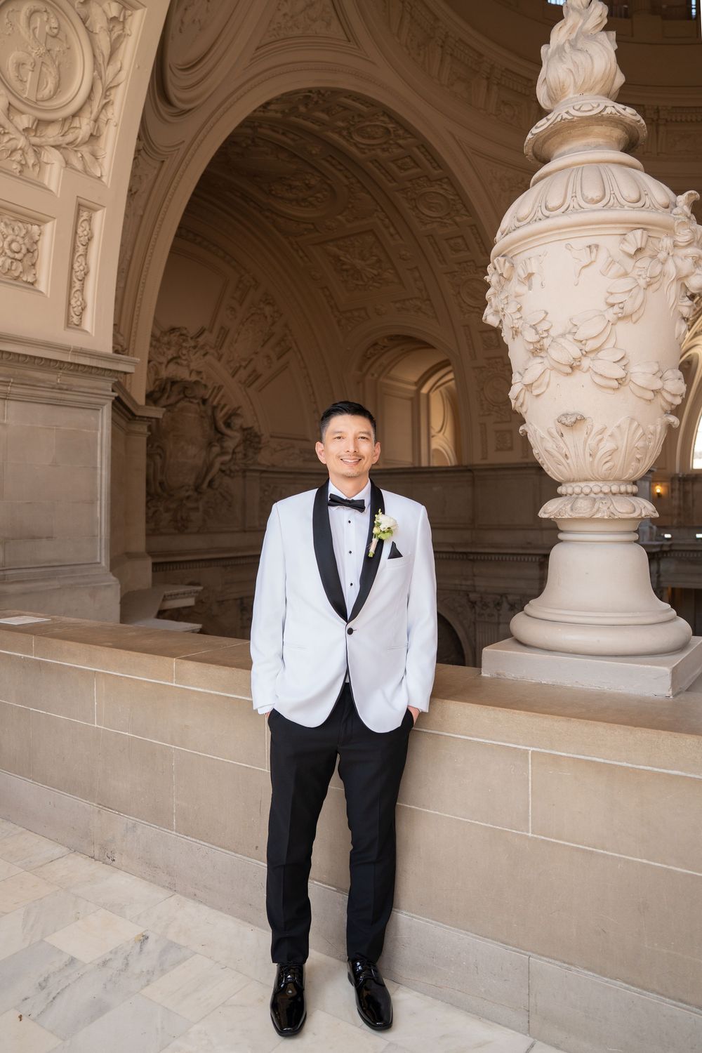 White-vested formal attire photographed against ornate classical architecture and stone sculptures.